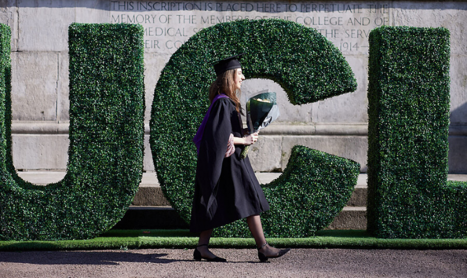 ӰԺ graduate walks past big green "ӰԺ" letters.